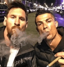 a man with a beard is smoking a cigarette next to another man .