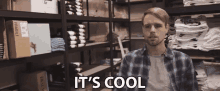 a man in a plaid shirt says it 's cool in front of a stack of fragile boxes