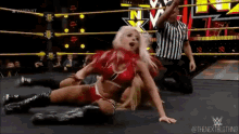 a woman is laying on the ground in a wrestling ring while a referee watches .