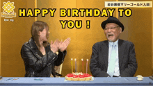 a man and a woman are sitting at a table with a cake and candles and a happy birthday to you sign
