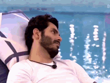 a man with a beard is laying in front of a pool with the letter b on the bottom right