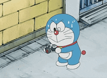 a cartoon of doraemon holding a camera in front of a brick wall