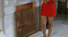 a woman in a red dress stands in front of a fireplace
