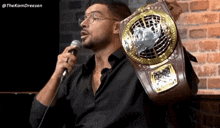 a man in a black shirt is holding a championship belt in front of a microphone