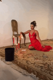 a woman in a red dress is kneeling on the floor next to candles and a chair