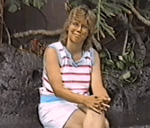 a woman wearing glasses and a striped shirt is sitting on a rock