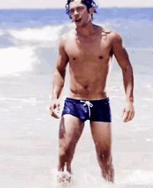 a shirtless man in blue swim trunks is standing in the water