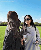 two women wearing sunglasses are standing next to each other in a grassy field
