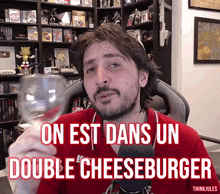 a man in a red shirt is holding a glass of wine with the words on est dans un double cheeseburger above him