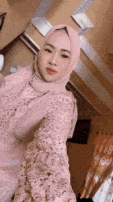 a woman wearing a pink hijab and a lace dress is taking a selfie .