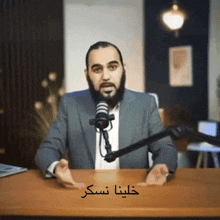 a man with a beard is sitting at a desk in front of a microphone with arabic writing on it