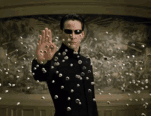 a man in a black suit and sunglasses is surrounded by balls that are falling