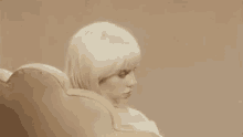 billie eilish is sitting in a chair with her head resting on the arm of the chair .