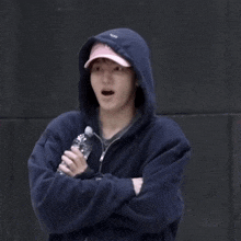 a man wearing a blue hoodie and a pink hat is holding a water bottle