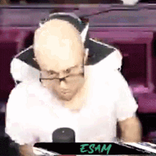 a bald man wearing glasses and headphones is sitting in front of a sign that says " exam "