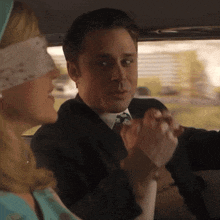 a man in a suit and tie is holding hands with a blindfolded woman