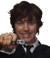 a man in a suit and tie is pointing at the camera while holding a watch in his hand .