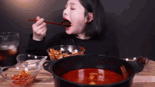 a woman is eating a bowl of food with chopsticks and a pot of food .