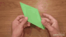 a person is folding a piece of green paper with the words made in animotica visible