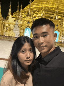 a man and a woman pose in front of a golden building