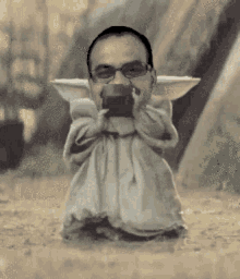 a man in a baby yoda costume is drinking from a mug .