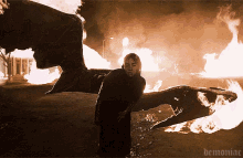 a demon with wings is standing in front of a fire with demoniac written on the bottom
