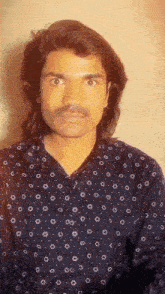 a man with long hair and a mustache is wearing a black shirt with polka dots .
