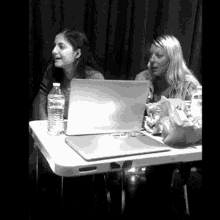 two women are sitting at a table with a laptop and a water bottle
