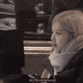 a woman with a scarf around her neck is sitting in front of a computer screen with the words but the entire song below her