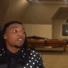 a man in a polka dot jacket is sitting in front of a pool table and making a funny face .