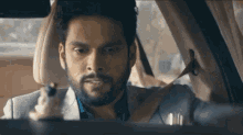 a man with a beard is sitting in the driver 's seat of a car looking out the window .