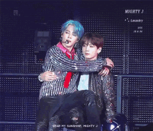 a man with blue hair is hugging another man with black hair on stage .