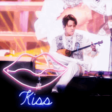 a man playing a guitar in front of a neon sign that reads kiss