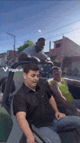 a man in a black shirt is sitting in a vehicle with a man in a yellow shirt on the back