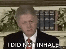a man in a suit and tie is sitting in front of a bookshelf .