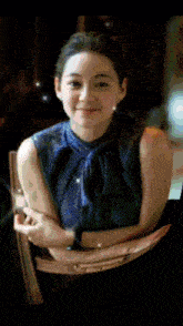 a woman in a blue top is sitting in a chair with her arms crossed