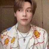 a young man wearing a white shirt and a necklace is looking at the camera .