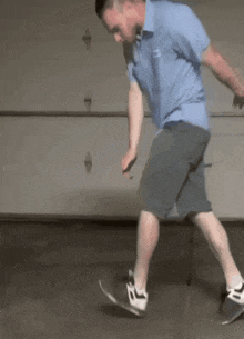 a man in a blue shirt and grey shorts is riding a skateboard