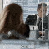 a man in a suit and tie is talking to a woman who is sitting at a desk and the woman says donna