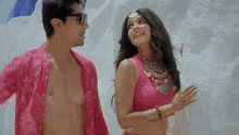 a man and a woman are standing next to each other on a beach . the woman is wearing a pink top .