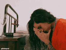 a woman covering her face with her hands next to a book and a wine glass