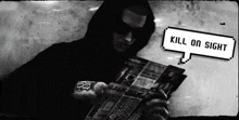a man in a black hoodie is reading a newspaper .