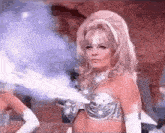 a woman in a silver bra and gloves is standing in front of a blue light .