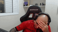 a bald man wearing headphones and a maxracer chair