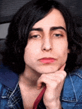 a young man with long hair is holding his hand to his chin .