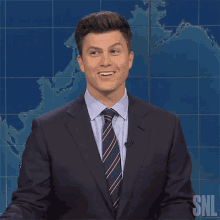 a man in a suit and tie stands in front of a snl sign
