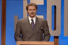 a man in a suit and tie is standing at a podium with his hands in his pockets .