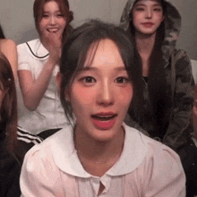 a group of young women are sitting in a room and one of them is wearing a hooded jacket