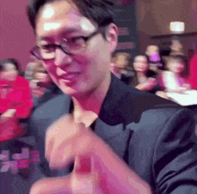 a man wearing glasses and a black suit is giving a thumbs up