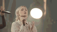 a woman singing into a microphone with a person holding a microphone behind her